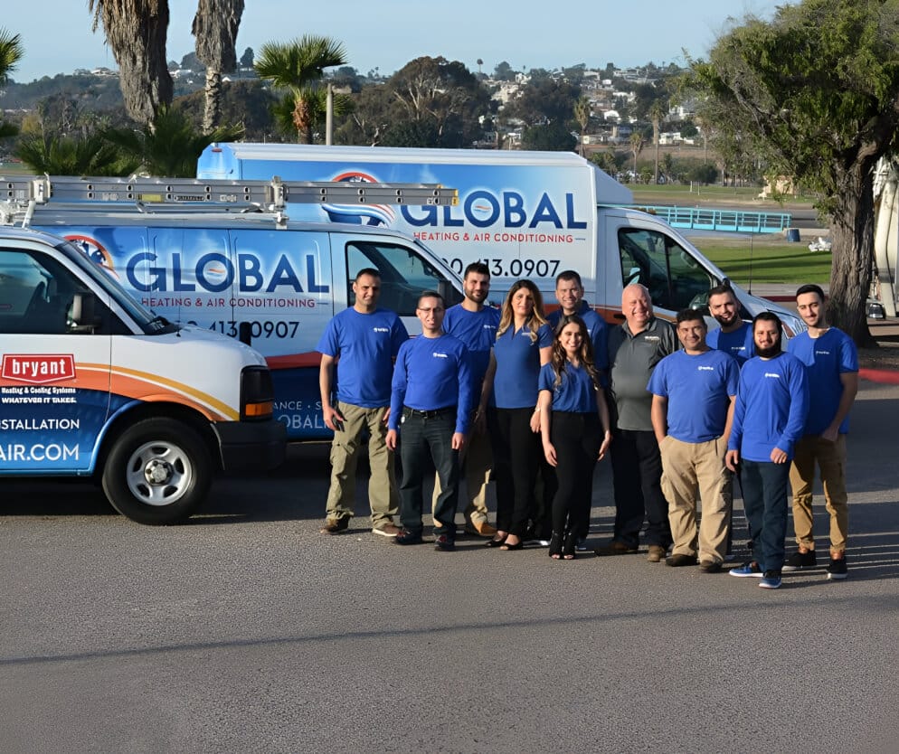 A team of professionals in blue shirts stands in front of branded HVAC service vehicles.