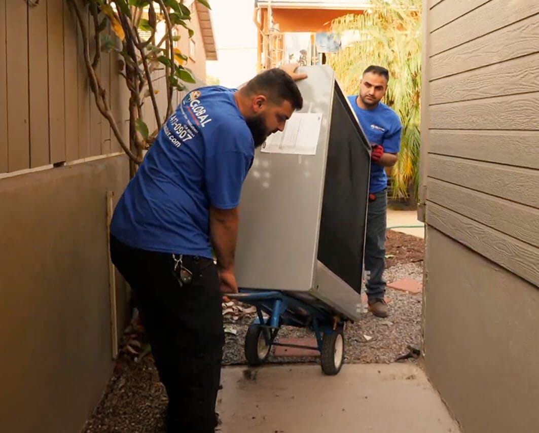 Two workers in blue shirts transport a large appliance.